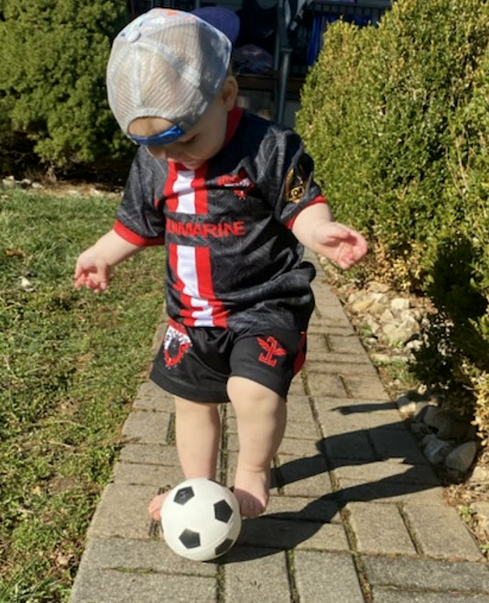 A young Valhalla in the black and red kit striking a ball on a brick path